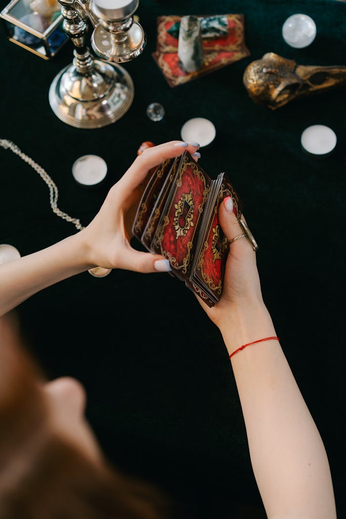 A woman's hands are seen shuffling tarot cards on a table surrounded by candles, creating an aura of mystery and divination.